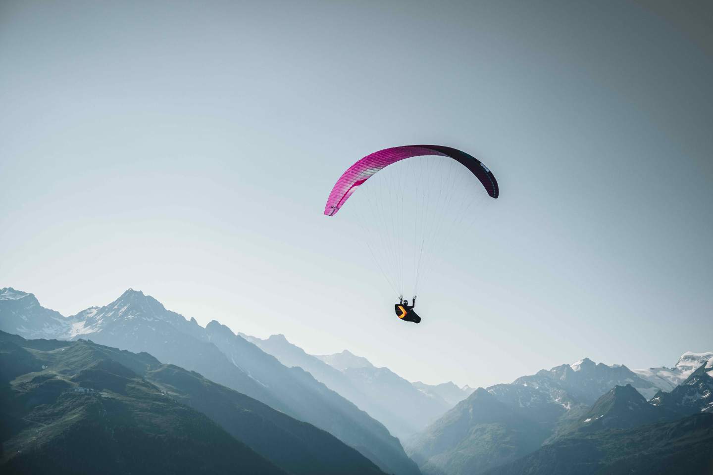 Parapentiste seul en vol au-dessus d’un versant alpin isolé, sans atterrissage aménagé visible en contrebas.