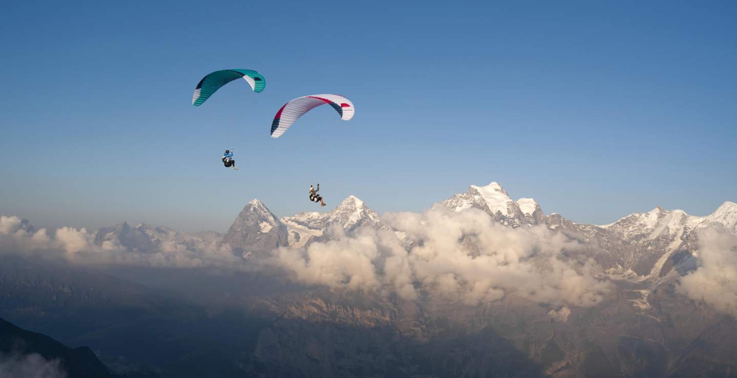 Pilote portant une aile de parapente pliée dans son sac lors d’une montée à pied en montagne, prêt à décoller depuis le sommet