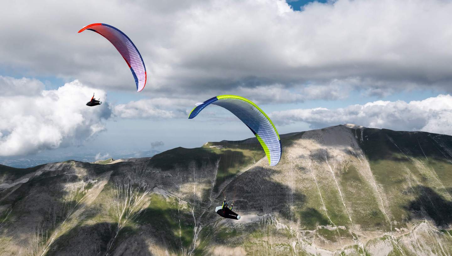 Parapentiste en vol au-dessus d’un relief de montagne, aile légère gonflée dans un ciel de fin de journée
