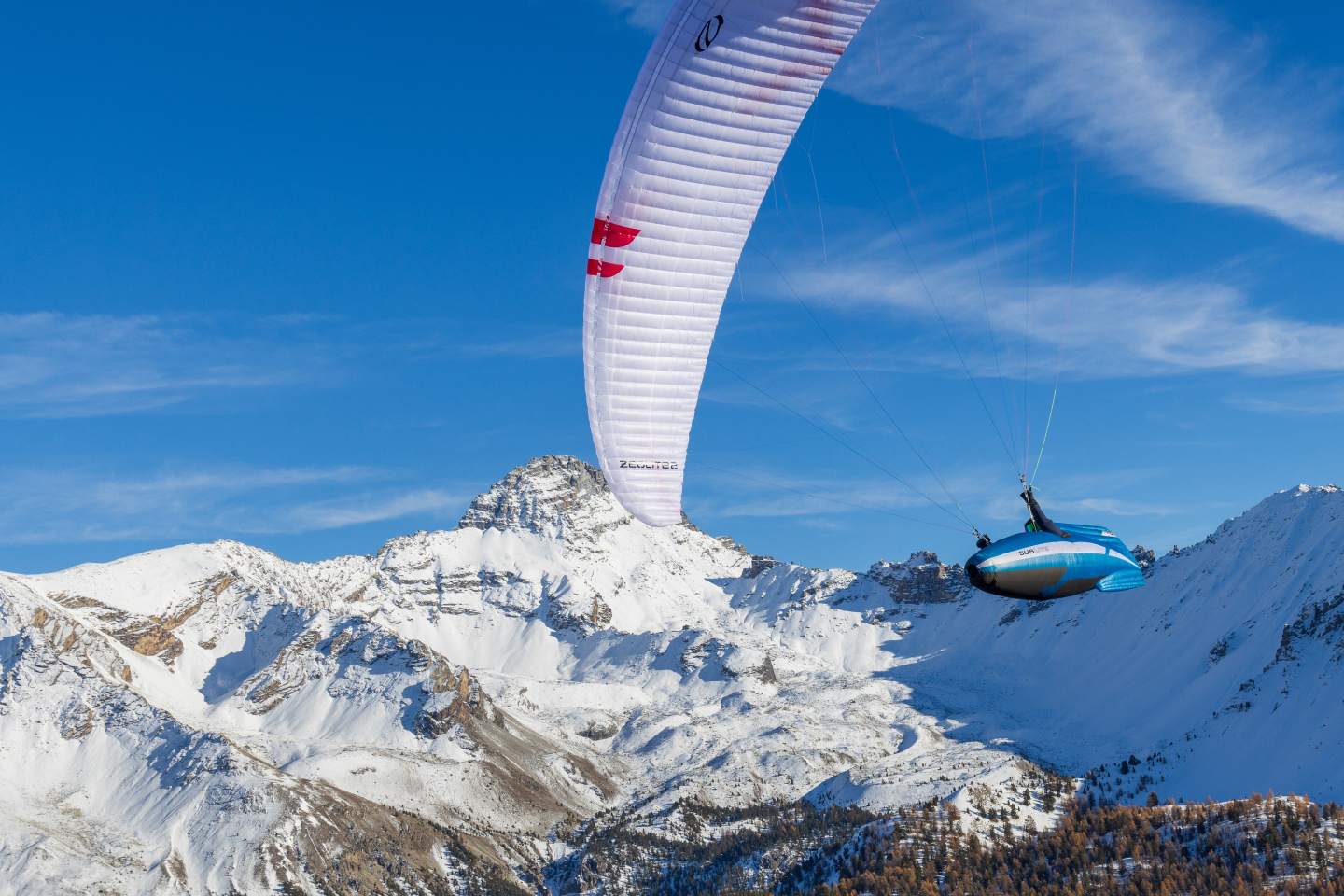 Pilote de parapente sous une aile légère de hike & fly, en virage au-dessus d’un versant de montagne dans la lumière du matin