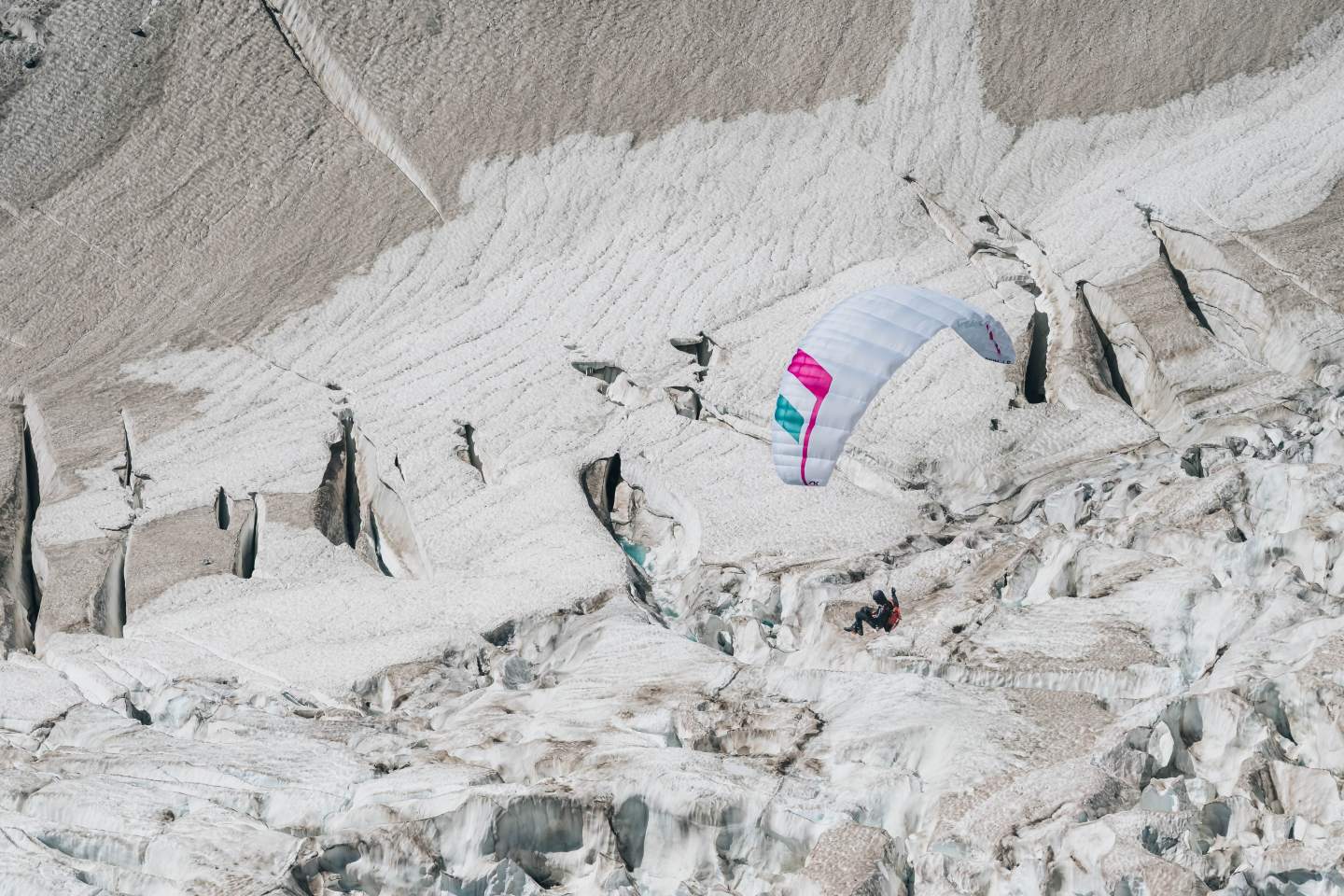 Pilote en parapente léger survolant un relief alpin italien aux versants boisés et sommets rocheux