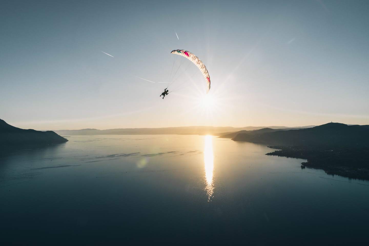Parapente léger de couleur vive prêt au décollage sur une pente d’altitude, matériel de hike & fly posé au sol devant un panorama de montagne.